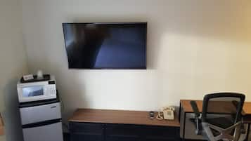 Una habitación de hotel pequeña con televisión de pantalla plana montada en la pared, una kitchenette con microondas, un escritorio de madera, una silla y un teléfono.