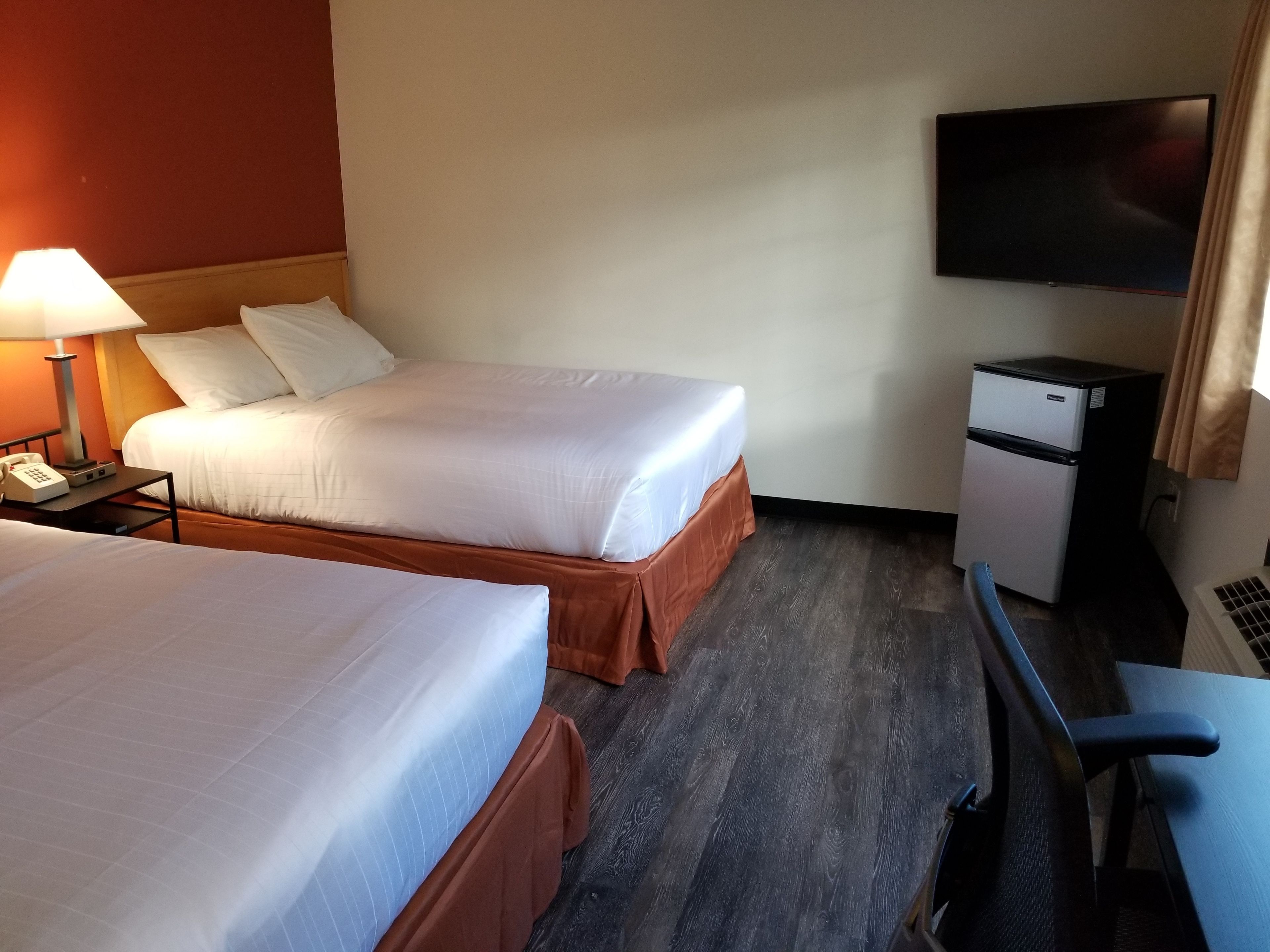 A hotel room with two beds, a desk, a television, and a minibar.