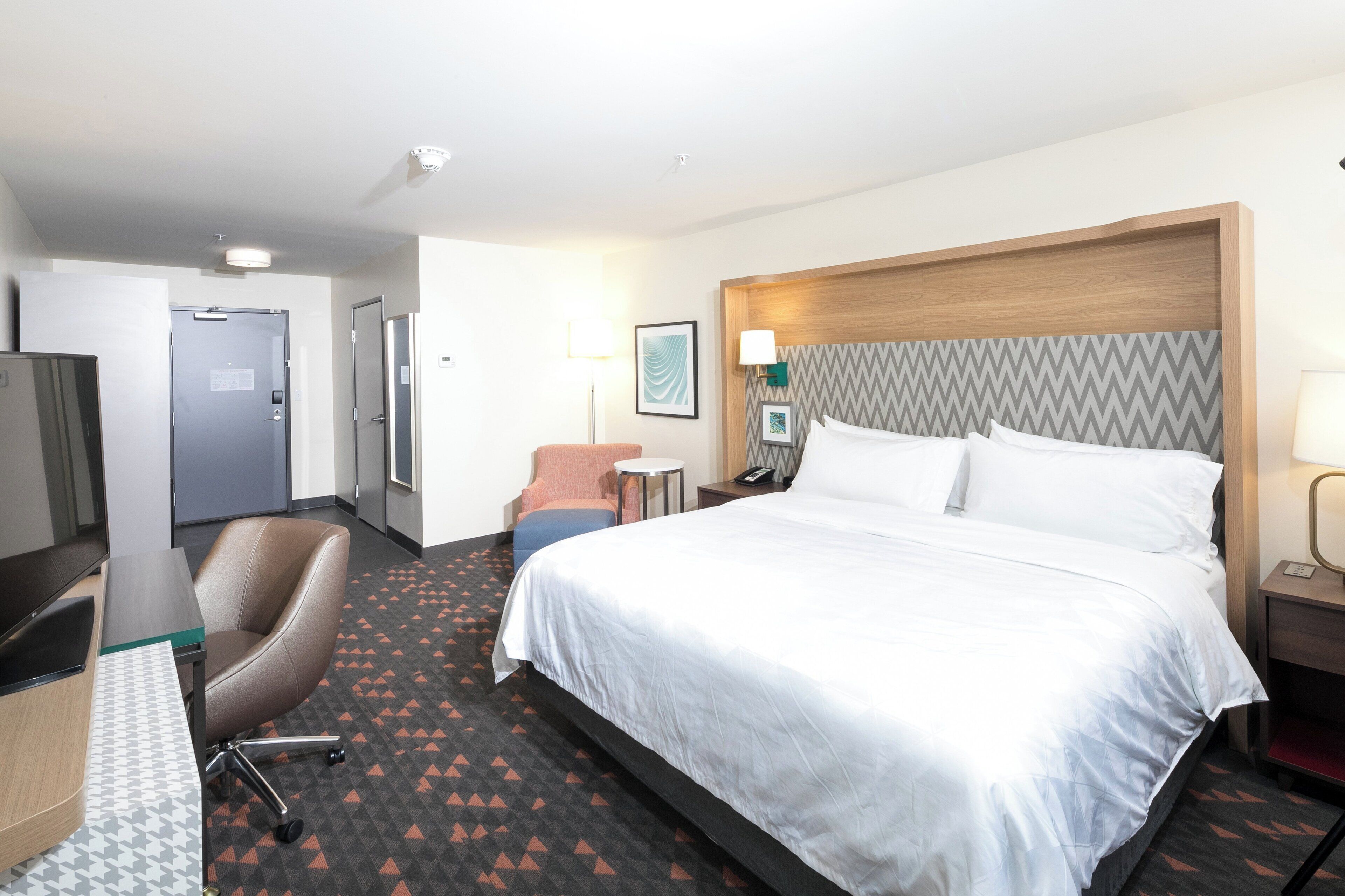 Une chambre d’hôtel avec un grand lit, un bureau avec une chaise, une petite table et une chaise.