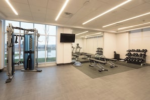 A gym with exercise equipment, a television, and a view of a body of water through large windows.