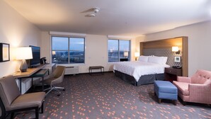 A hotel room with a bed, desk, chairs, and large windows. - Holiday Inn Kalamazoo West by IHG (Kalamazoo)