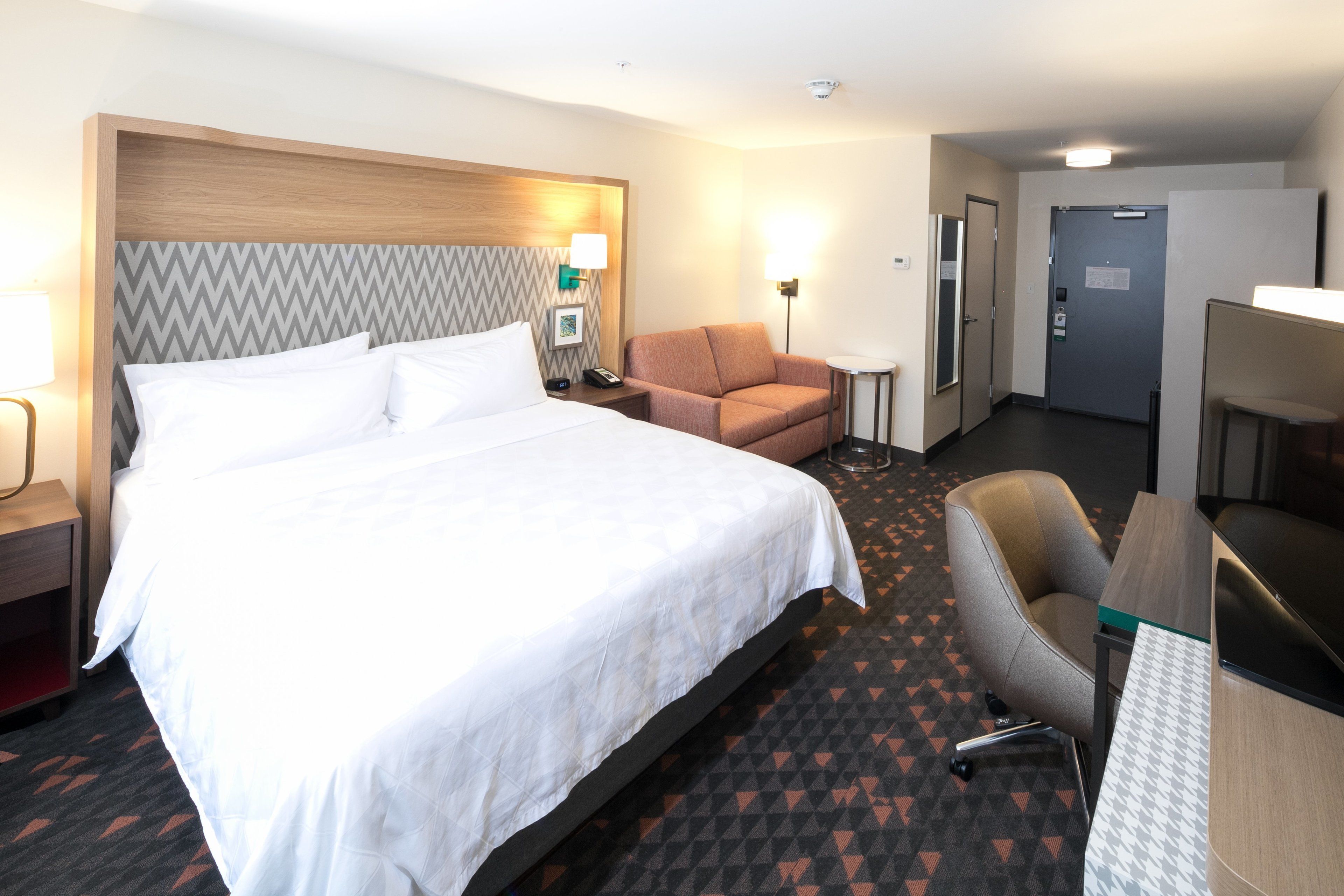 A hotel room with a large bed, a desk, a chair, and a small table.