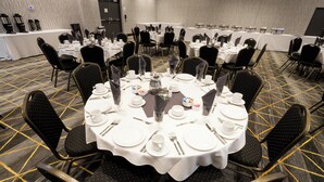 A conference room with round tables set for a meeting, equipped with nameplates, plates, cutlery, and glasses. - Holiday Inn Kalamazoo West by IHG (Kalamazoo)