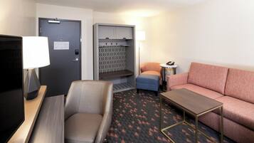 A hotel room with a bed, a sofa, a desk, a chair, a TV, a lamp, and a bathroom with a towel rack.