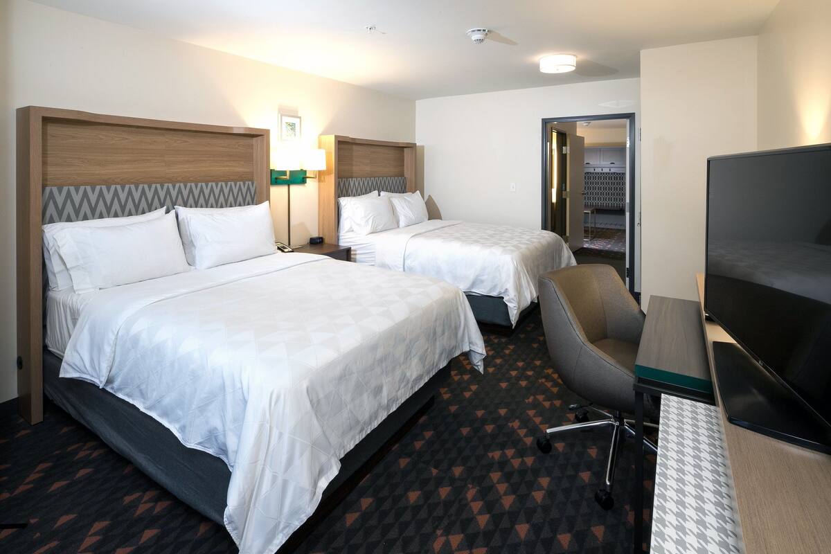 A hotel room with two beds, a desk, a chair, and a TV.