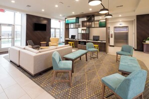 A modern lobby with a sofa set, armchairs, a desk, and a flat-screen TV. - Holiday Inn Kalamazoo West by IHG (Kalamazoo)
