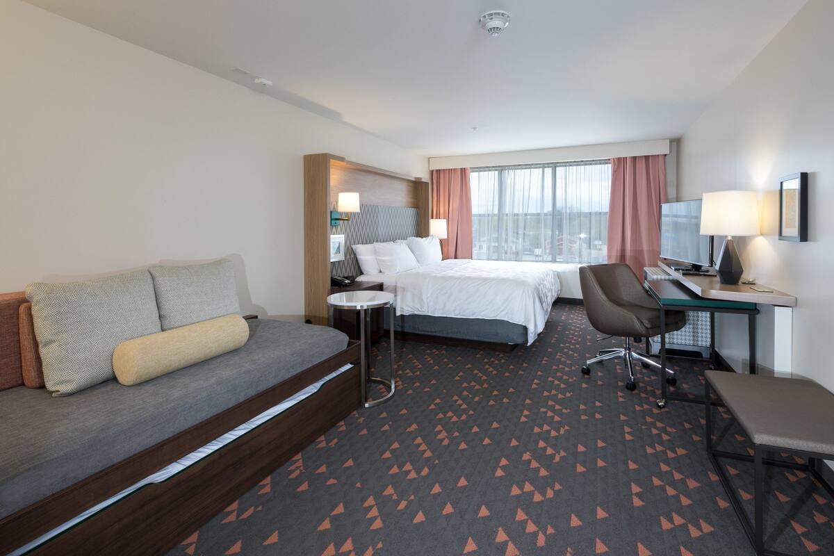 A hotel room with a bed, a desk, a chair, a sofa, and a small table.
