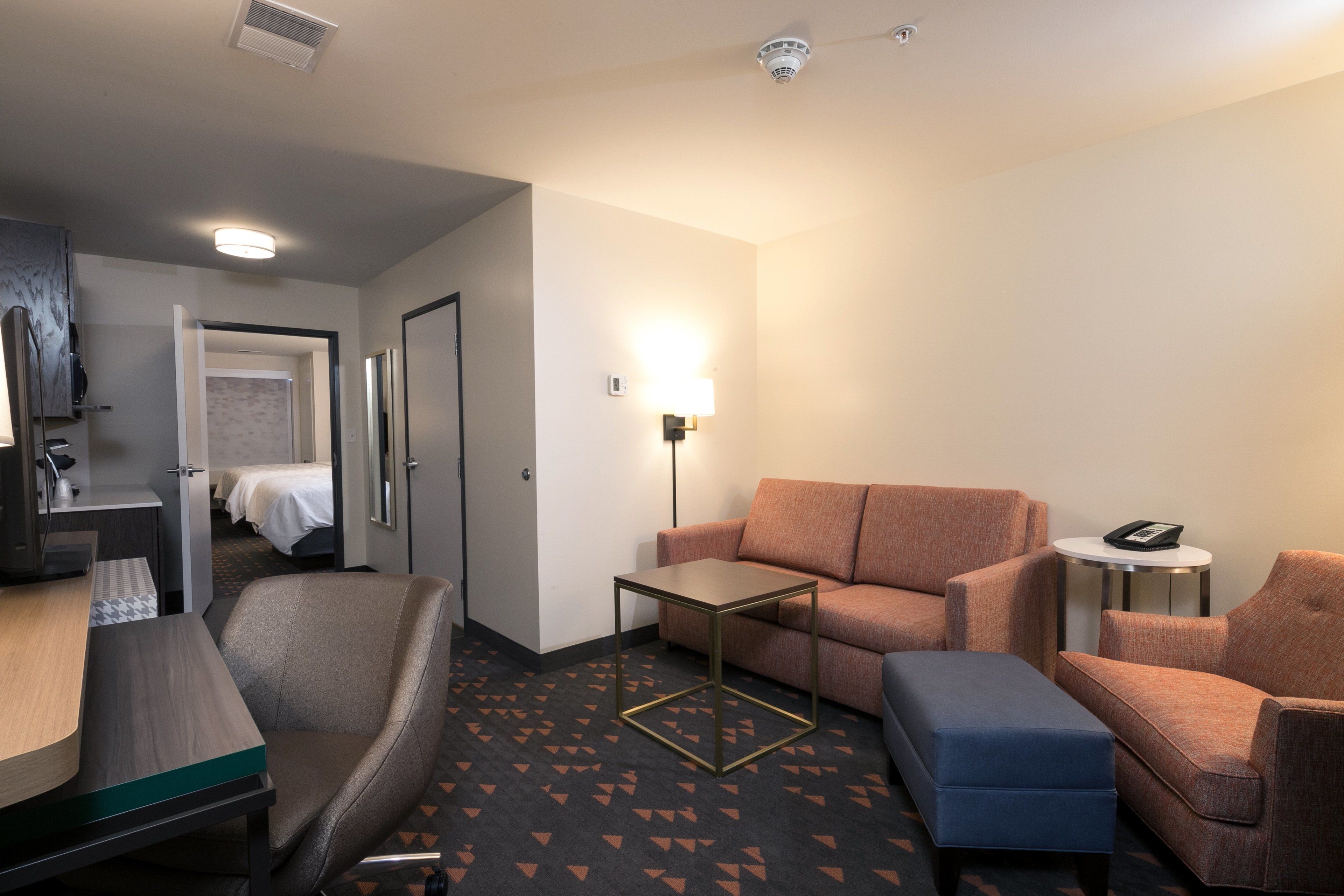 A hotel room with a bed, a desk, a sofa, a coffee table, and a small side table with a phone.