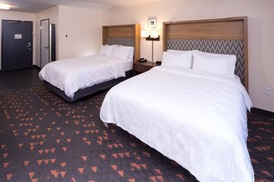 Habitación de hotel con dos camas, una alfombra de estampado geométrico, una lámpara de pared y una puerta con cerradura de seguridad.