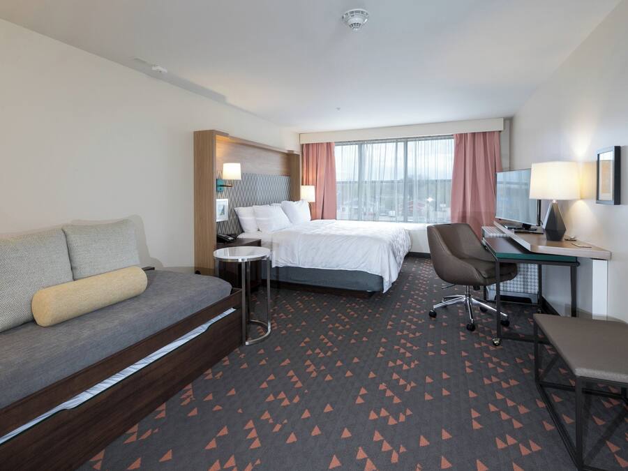 A hotel room with a bed, a desk, a chair, a sofa, and a window with curtains.