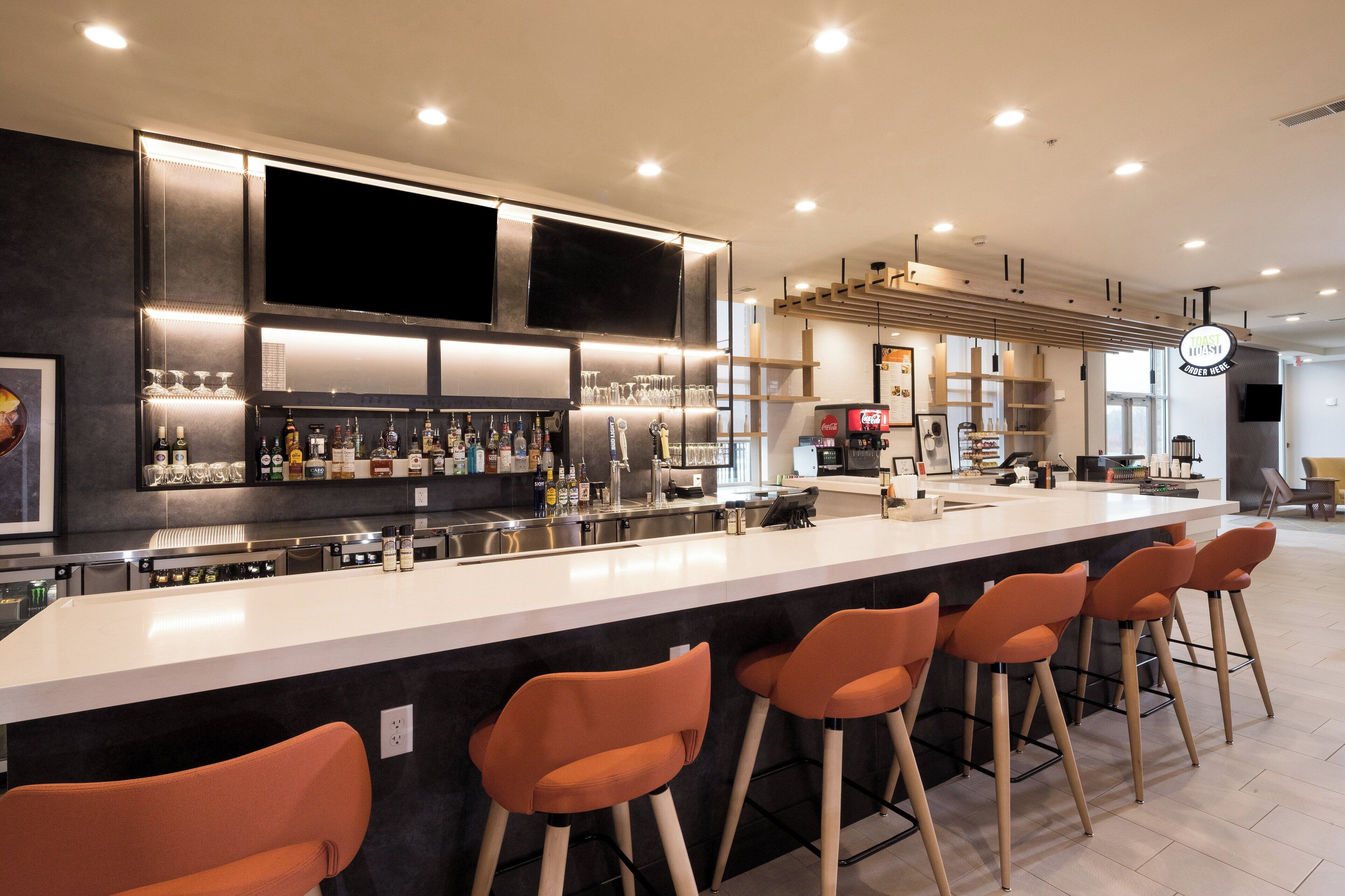A modern bar area with a long counter, bar stools, and a variety of bottles and glasses.