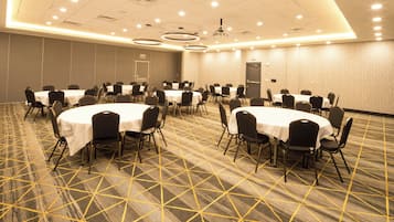 A conference room with round tables and chairs, carpeted floor, and a projector on the ceiling.