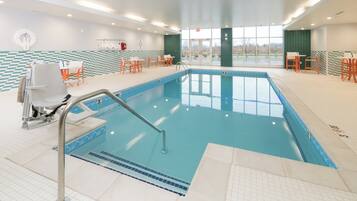 An indoor swimming pool with a diving board, lounge chairs, and a view of the outdoors.