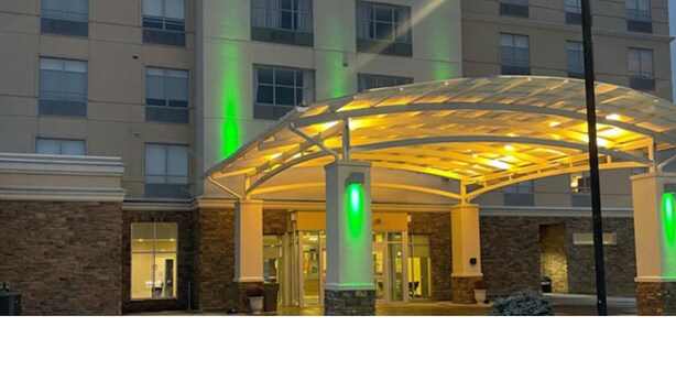 A hotel entrance with a covered walkway, stone facade, and illuminated green signs. - Holiday Inn Kalamazoo West by IHG (Kalamazoo)