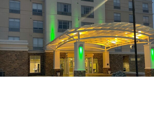 A hotel entrance with a covered walkway, stone facade, and illuminated green signs. - Holiday Inn Kalamazoo West by IHG (Kalamazoo)