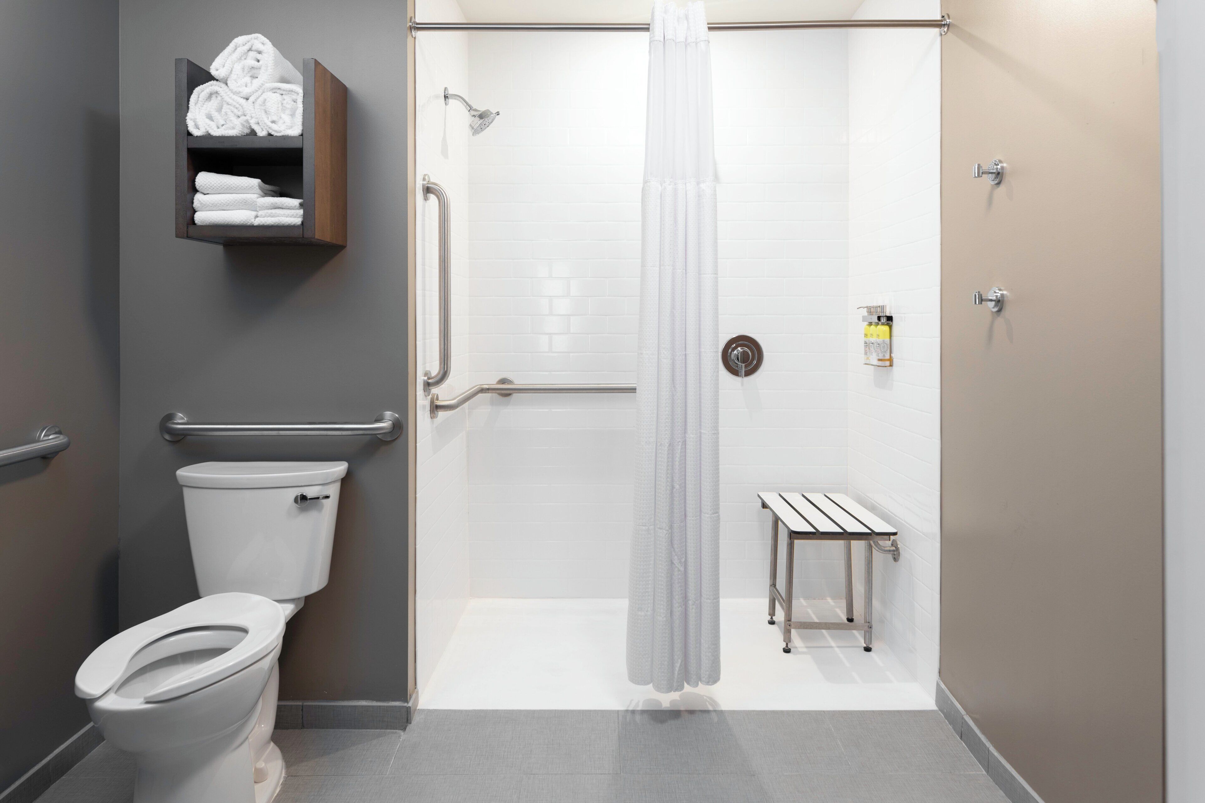 A modern bathroom with a toilet, shower, and a small bench.