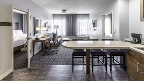 A modern hotel room with a bed, desk, chair, and kitchenette. - Staybridge Suites Montgomery - Downtown by IHG (Montgomery)