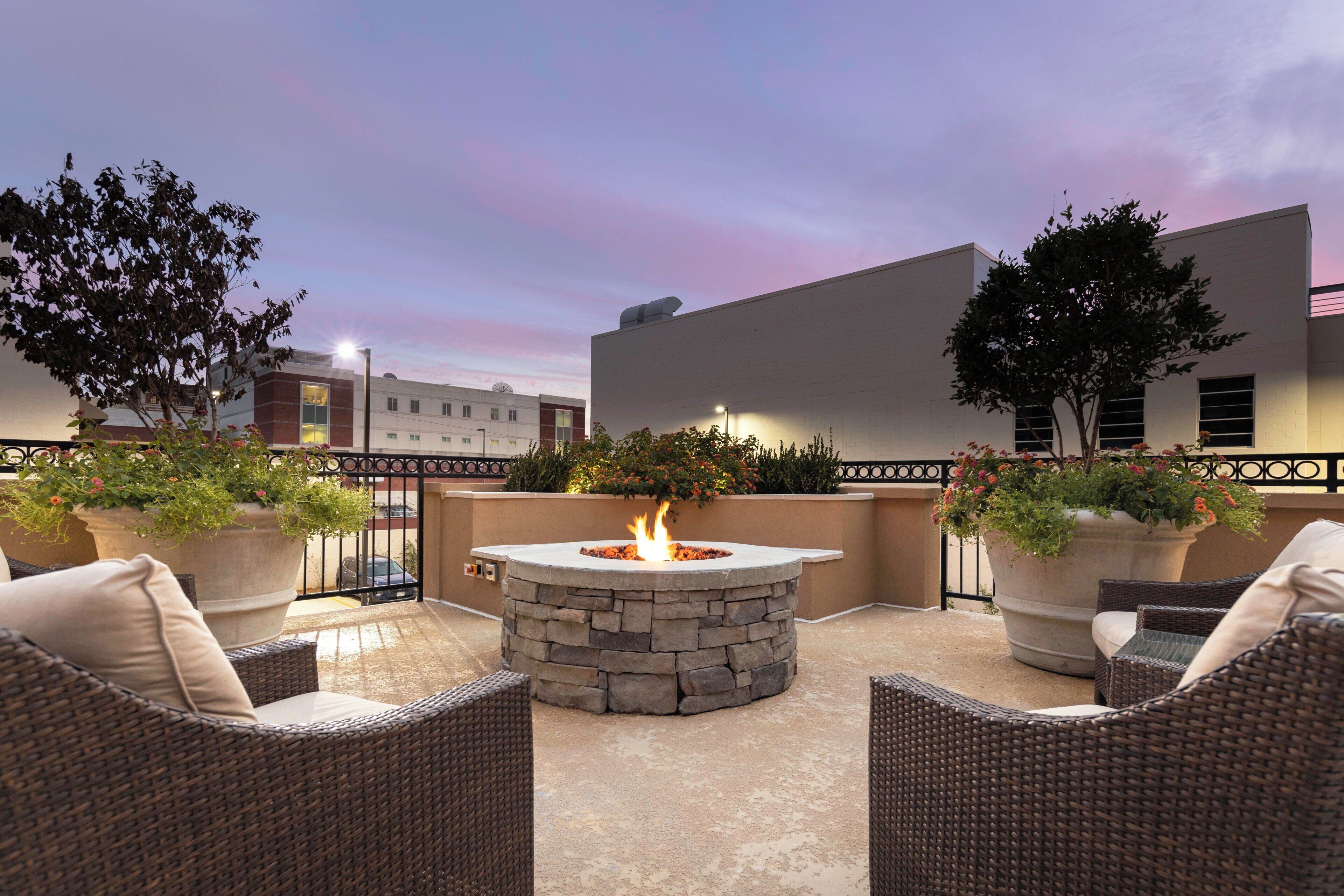 An outdoor patio area with wicker furniture, a stone fire pit, and potted plants.