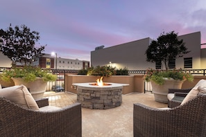 An outdoor patio area with wicker furniture, a stone fire pit, and potted plants. - Staybridge Suites Montgomery - Downtown by IHG (Montgomery)