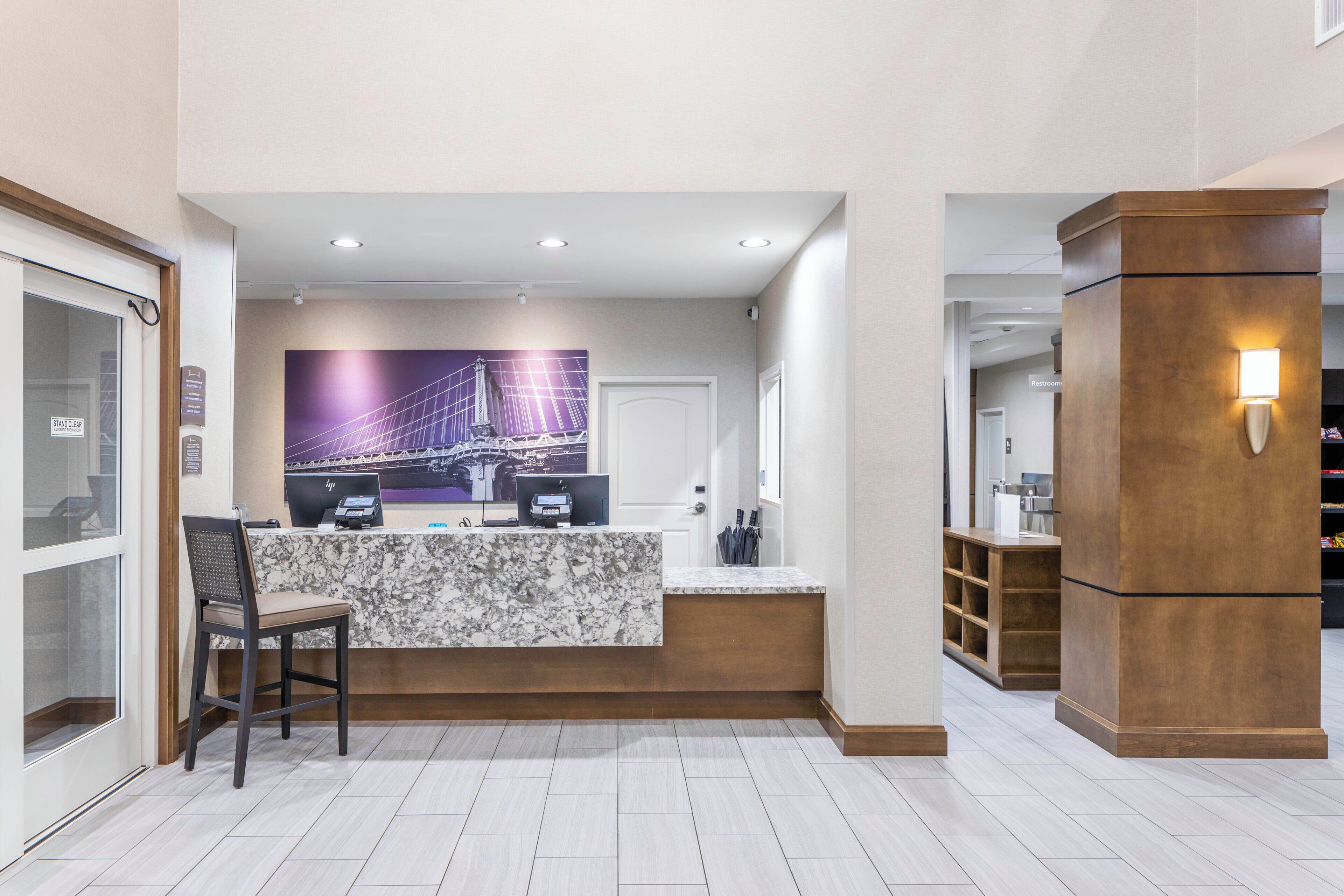 A reception area with a marble counter, a chair, a large framed picture of a bridge, and a wooden column with a light fixture.