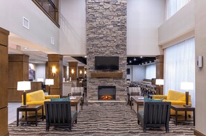 A lobby with a stone fireplace, seating area, and a TV mounted on the wall. - Staybridge Suites Montgomery - Downtown by IHG (Montgomery)