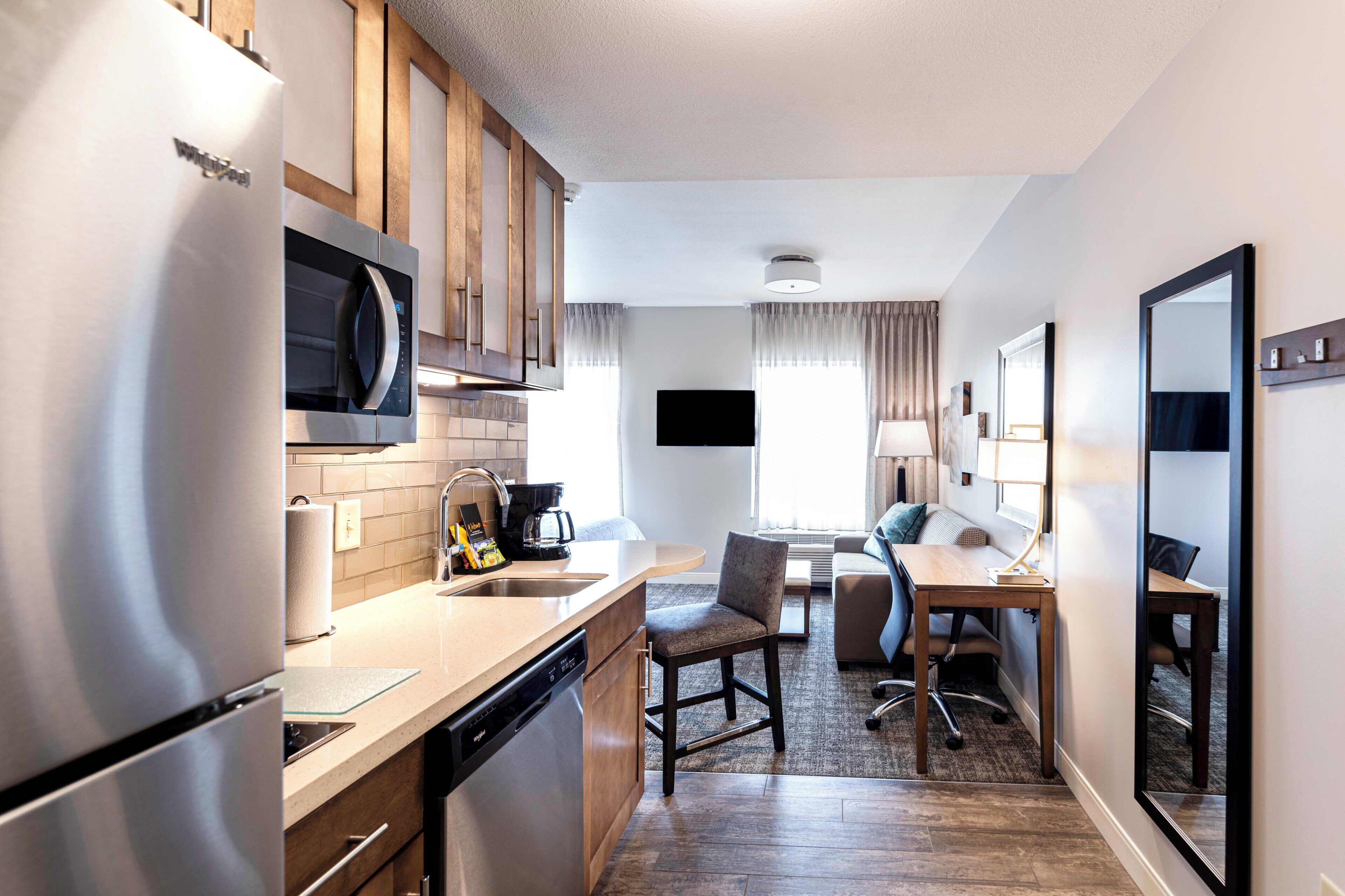 A compact hotel room with a kitchenette, a dining area, a seating space, and a large mirror.