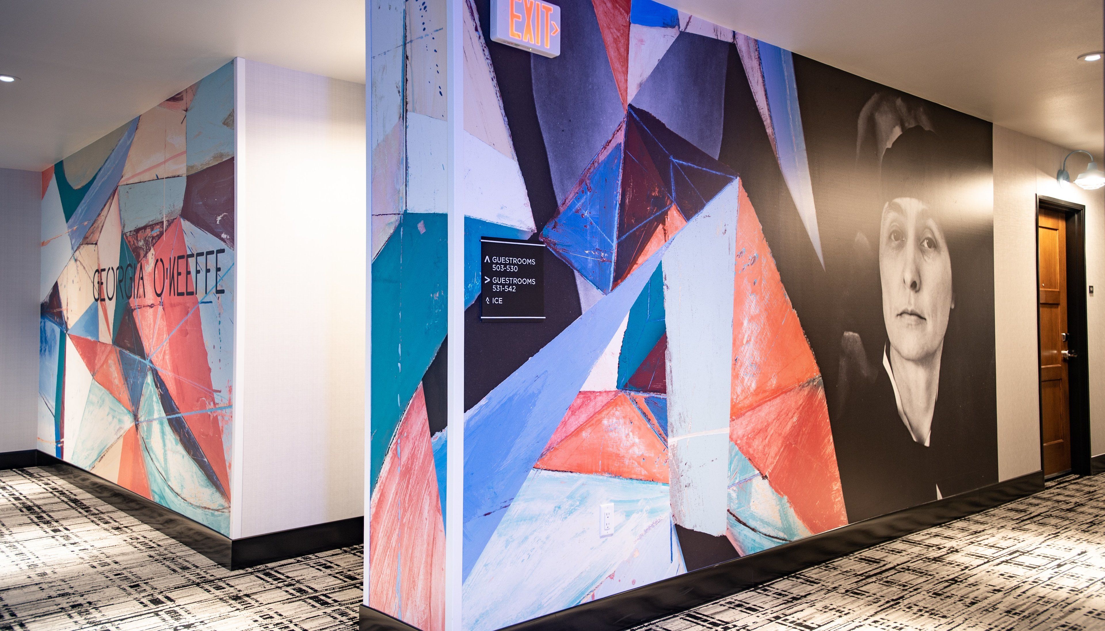 A hallway with geometric wall art and a door with a poster.