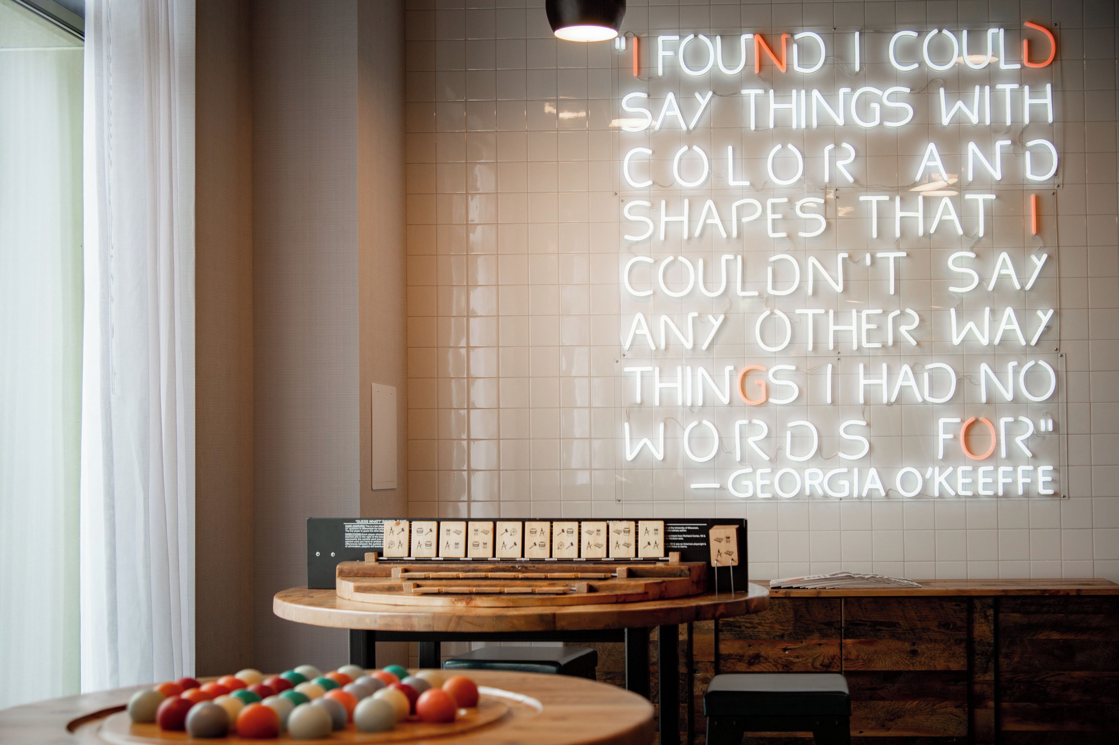 A room with a wall-mounted quote sign, a wooden table with a board game, and a window with curtains.