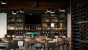 A bar area with multiple shelves of liquor bottles, glasses, and a television screen. There are several chairs and tables arranged for seating. - Hotel Indigo Madison Downtown by IHG (Madison)