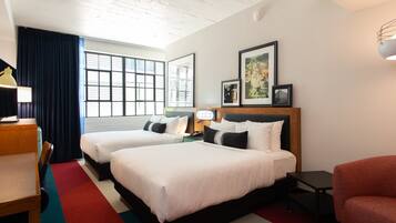 A hotel room with two beds, a desk, a chair, and a window with curtains.