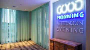 A hotel lobby with a neon sign reading 'GOOD MORNING APOSTOL EVENING' and a patterned carpet.