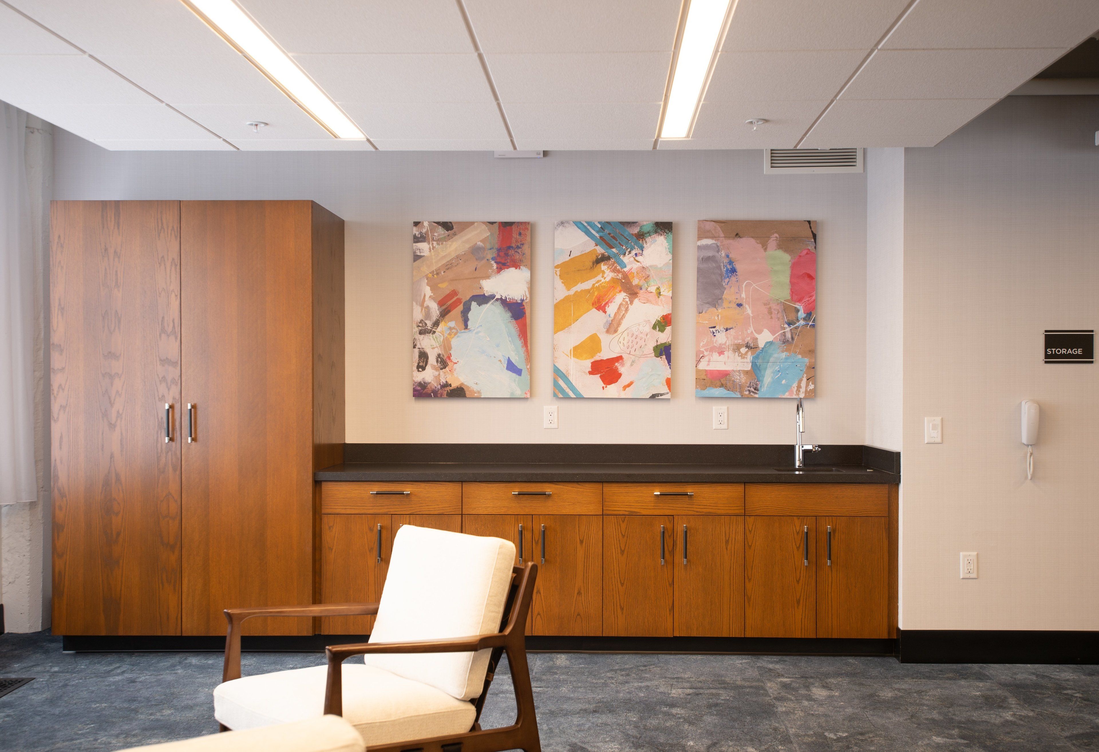 A waiting area with a wooden cabinet, a white cushioned chair, and abstract art on the wall.