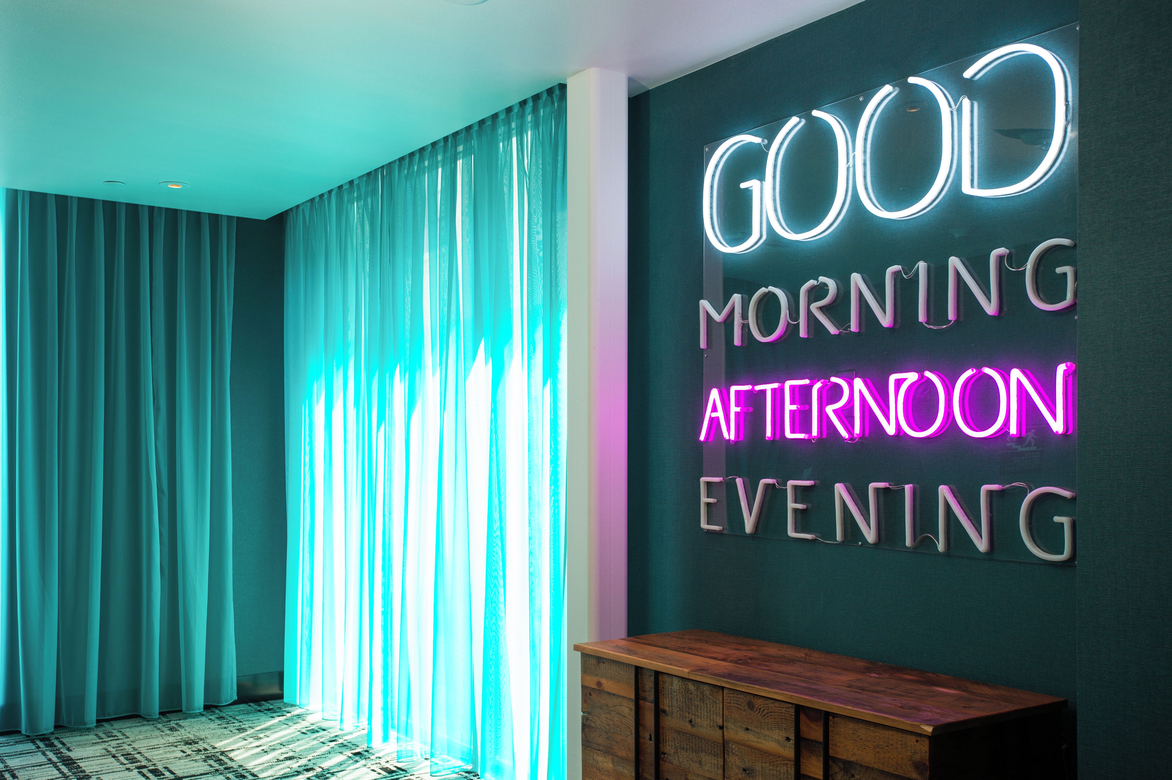 A room with teal curtains, a neon sign on the wall, and a wooden bench.