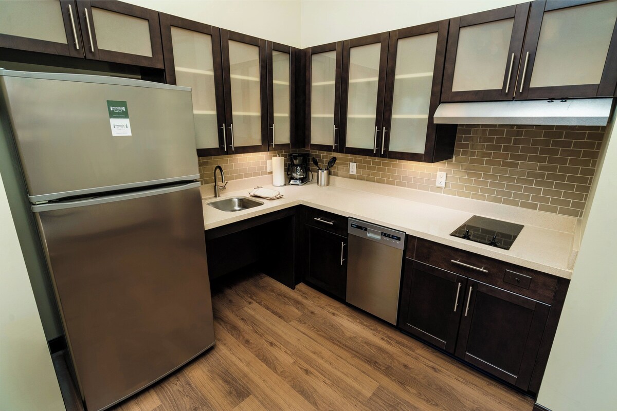 A modern kitchen with dark wooden cabinets, a stainless steel refrigerator, a dishwasher, and a tiled backsplash.