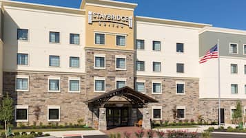 Un hotel Staybridge Suites con fachada de piedra, varias ventanas y una bandera estadounidense.