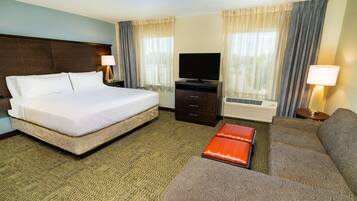 A hotel room with a large bed, a sofa, a TV, and a desk with drawers.
