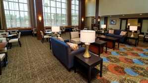 A spacious lobby with multiple seating areas, including sofas and chairs, arranged around a central coffee table. Large windows provide natural light, and the carpet features a geometric pattern. - Staybridge Suites Newark - Fremont by IHG (Newark)