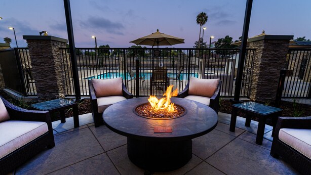 A patio area with a round table and chairs, a fire pit, and a view of a swimming pool. - Staybridge Suites Newark - Fremont by IHG (Newark)