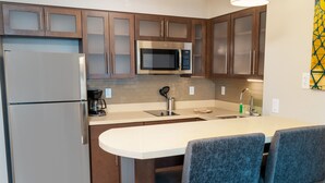 A modern kitchen with stainless steel appliances, wooden cabinets, and a central island with bar stools. - Staybridge Suites Newark - Fremont by IHG (Newark)