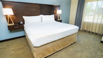 A neatly made bed with white linens, two bedside tables with lamps, and a large window with curtains.