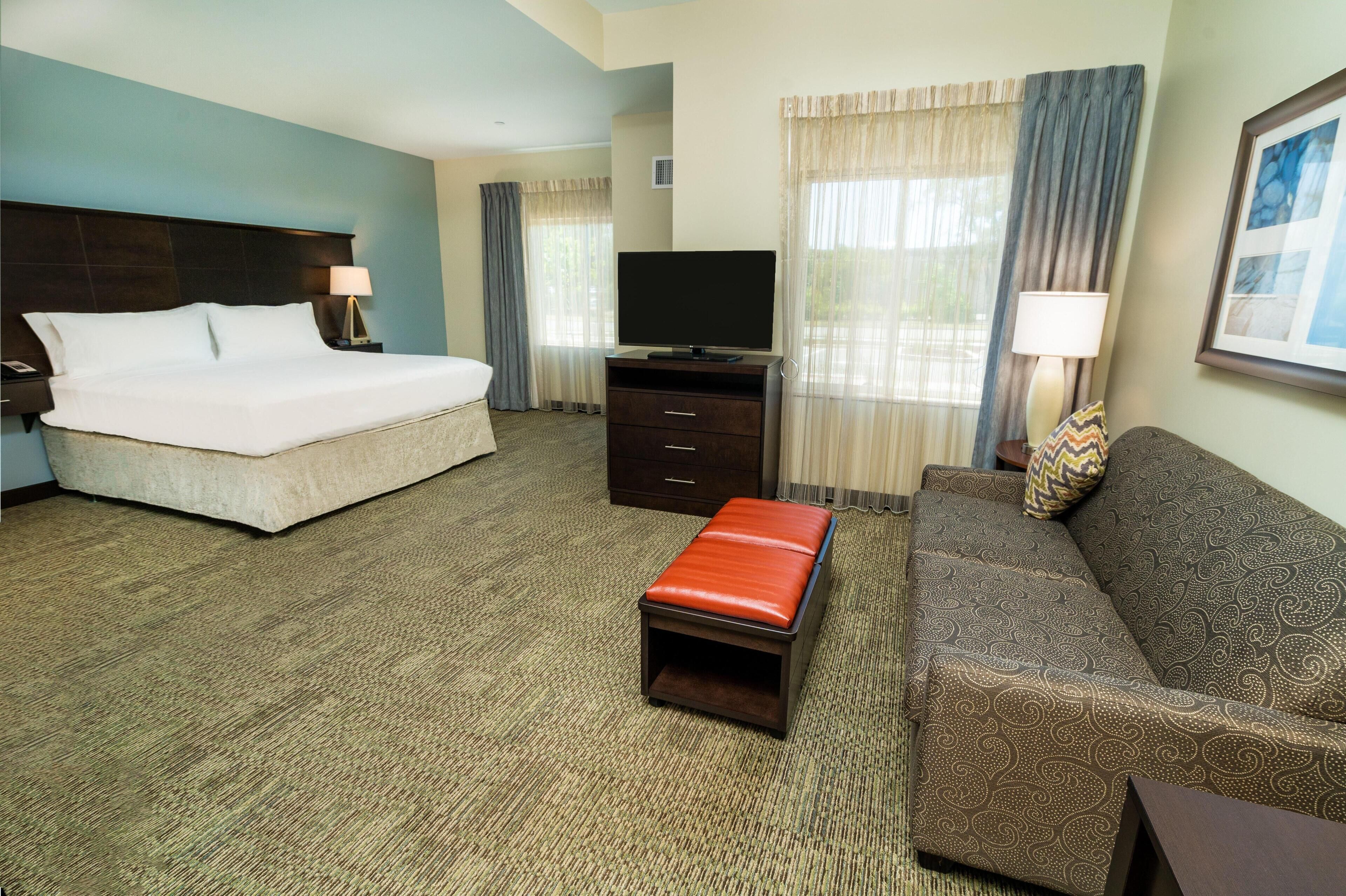 A hotel room with a bed, a TV, a sofa, a small table, and a carpeted floor.