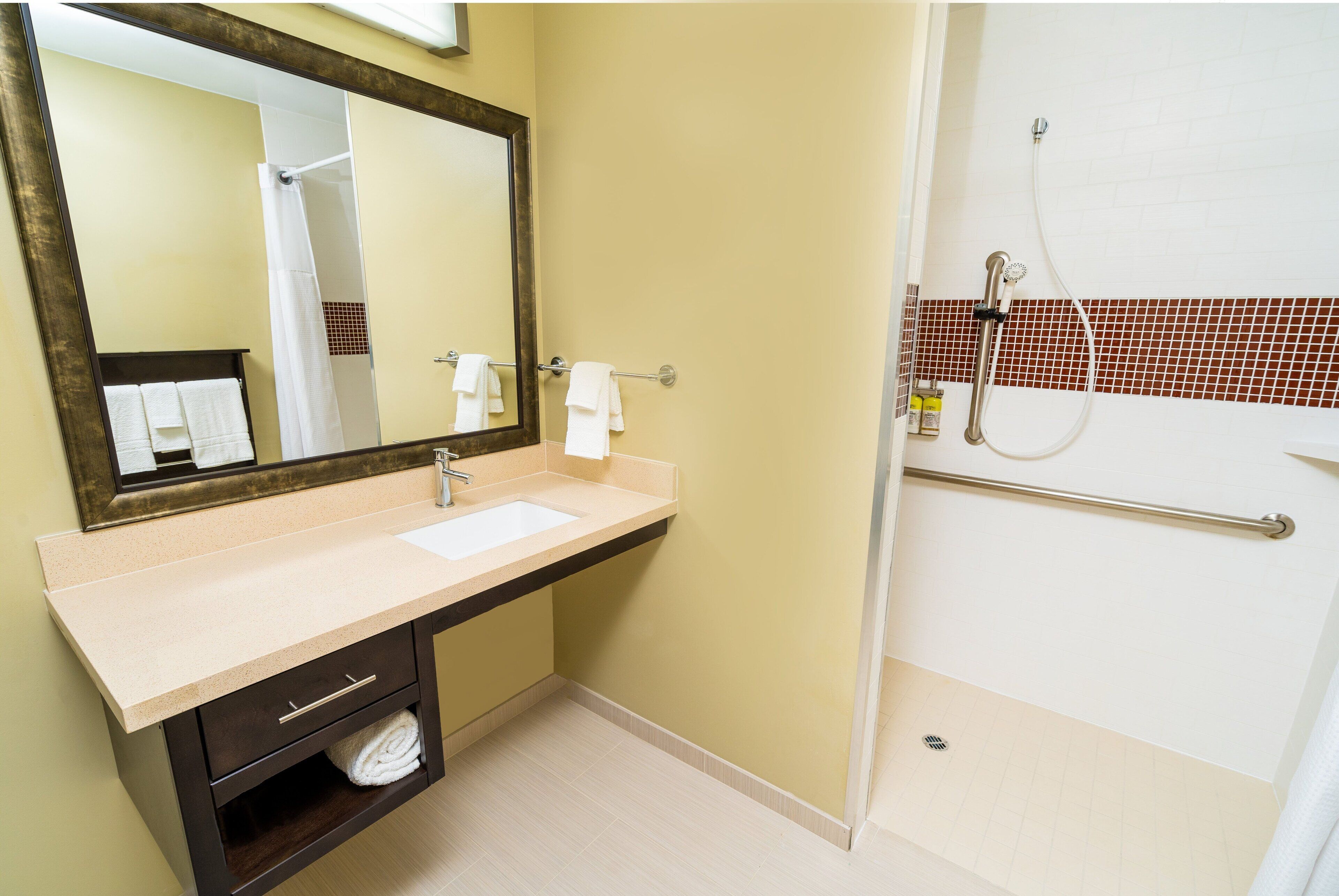 A bathroom with a sink, mirror, and shower.