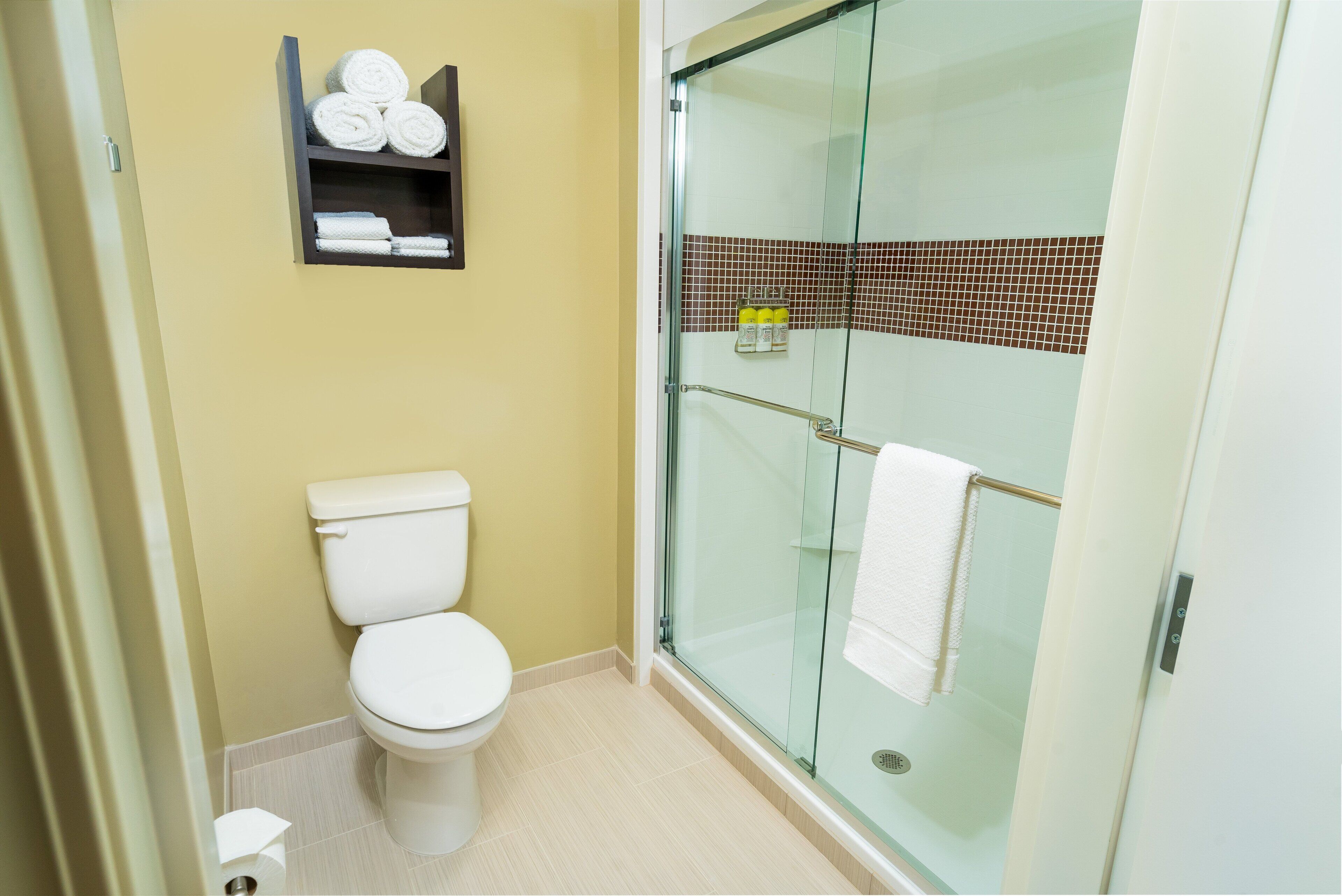 Une salle de bain comprenant des toilettes, une douche à parois de verre et une étagère avec des serviettes.
