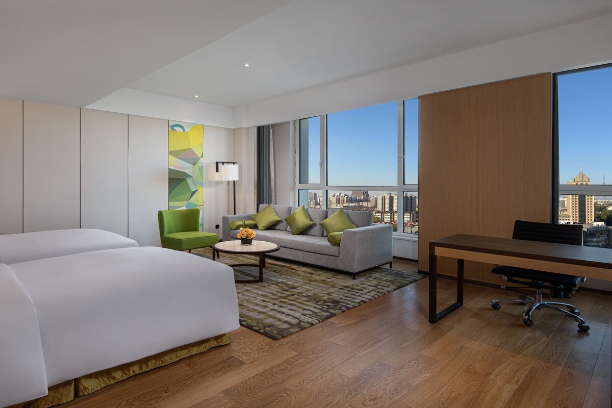 A hotel room with a large bed, a sofa, a desk, and a view of the city.