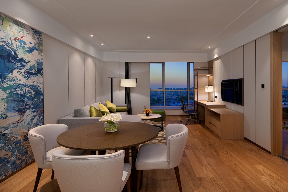 A modern living room with a dining area, large windows, and a city view.