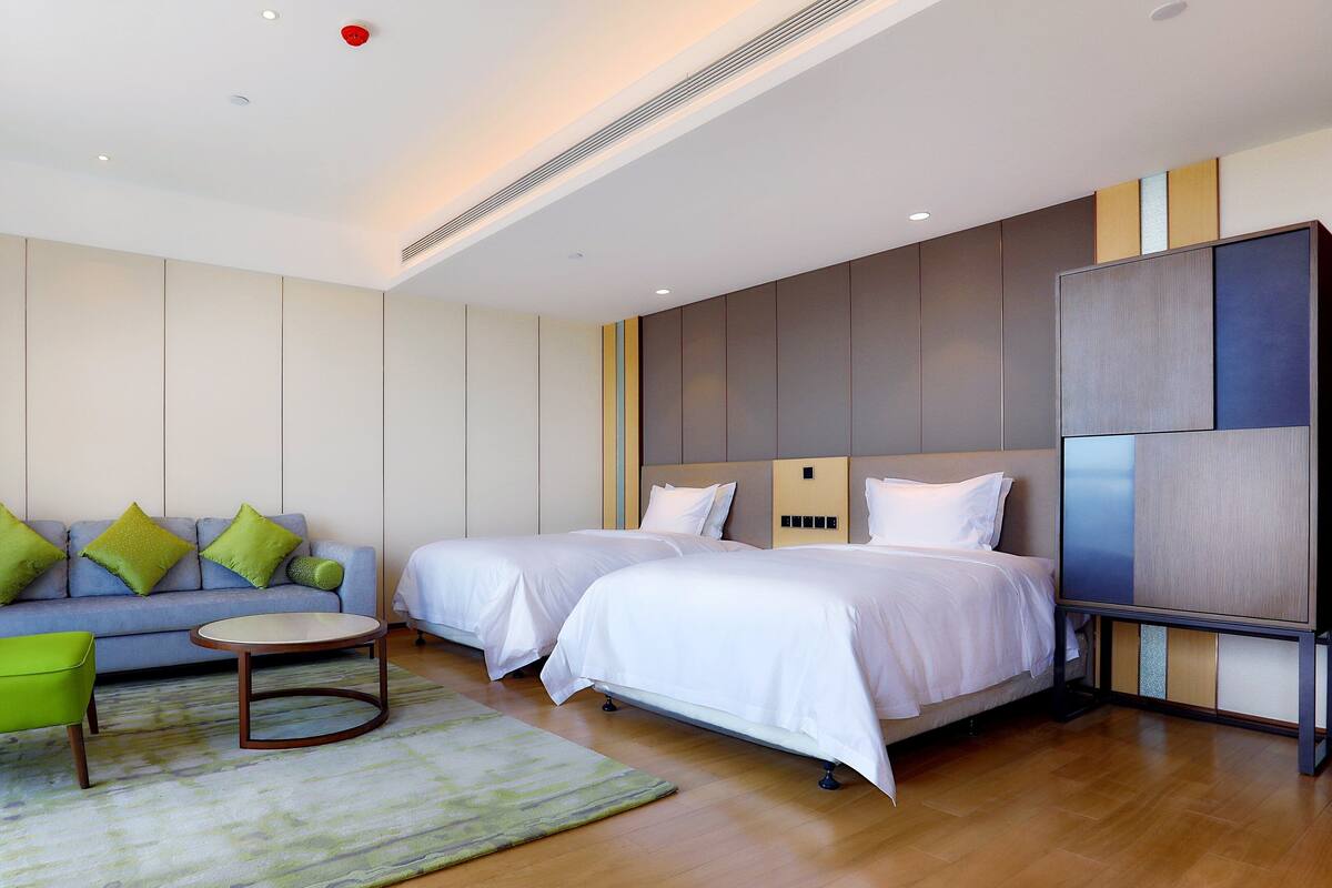 Een moderne hotelkamer met een bank, twee bedden, een tafeltje en een lamp.