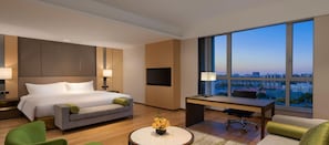 A hotel room with a bed, a desk, a chair, a TV, and a large window with a city view.