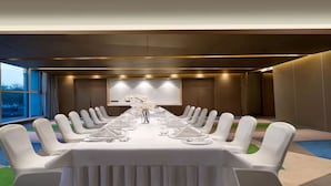 Une salle de conférence avec une longue table, des chaises blanches et un écran de projection.
