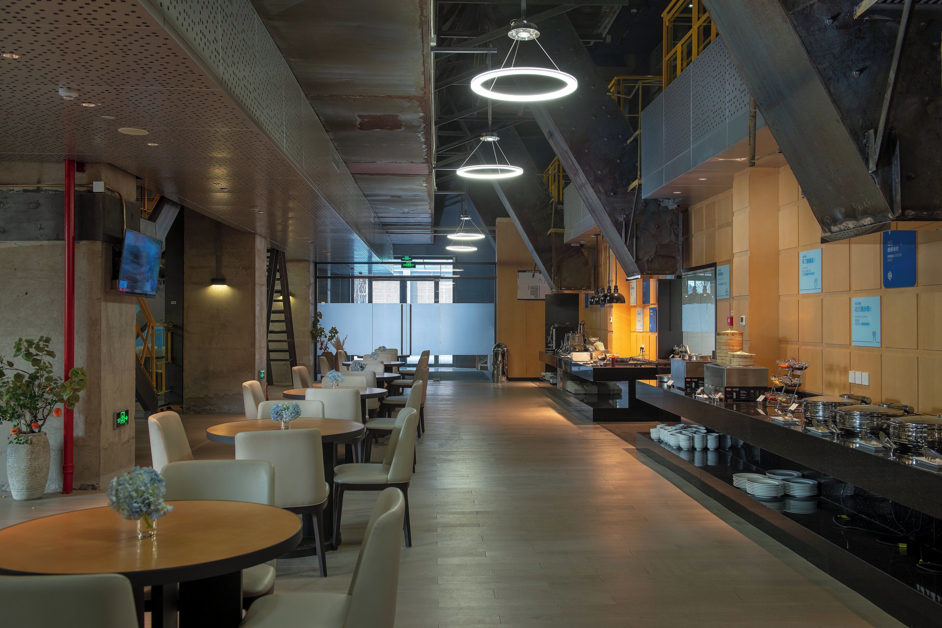 Un interior de restaurante moderno con techos altos, iluminación colgante y una zona de buffet.