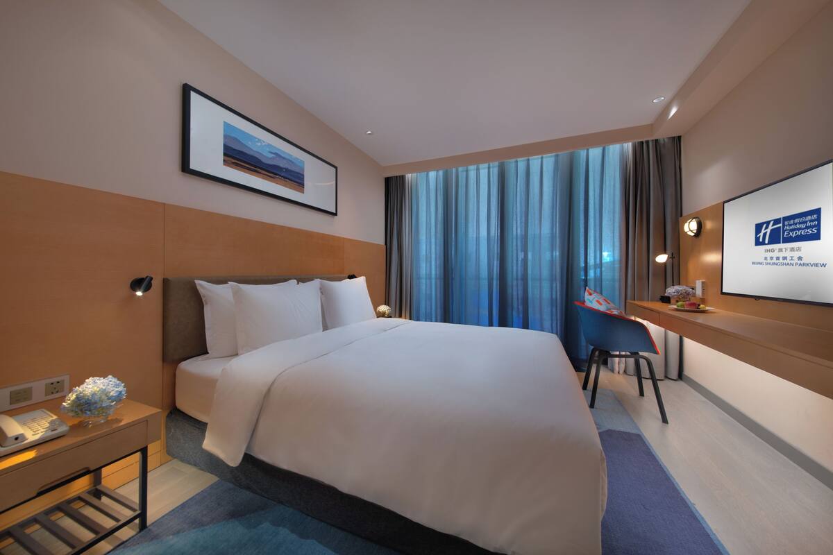 A hotel room with a large bed, a desk, a chair, a phone, and a framed picture on the wall.